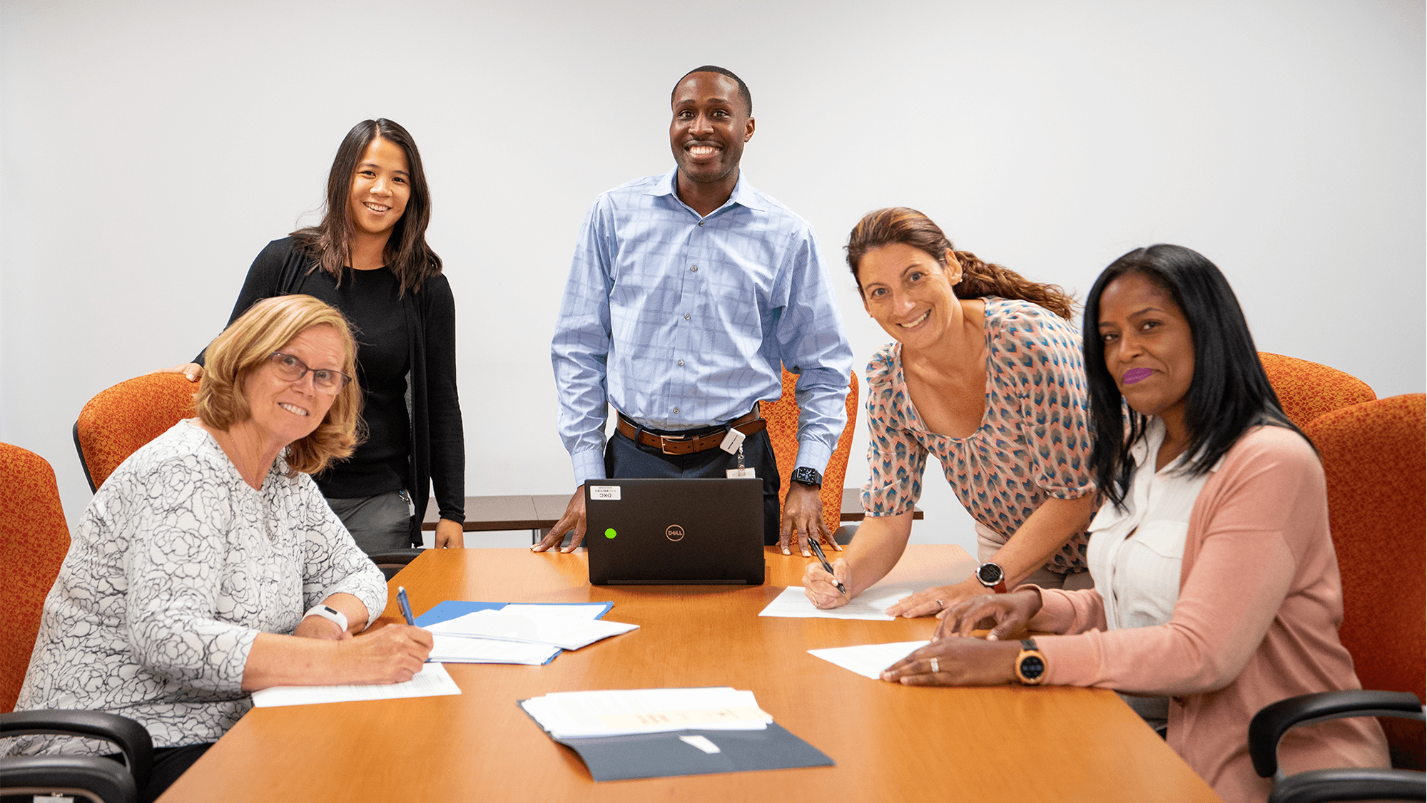 Employees smiling and working at a conference table.